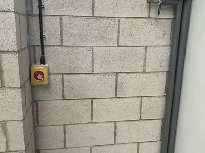 Bare block wall with existing pipes and electrical isolator before the wall-mounted pressure washer installation in Nottingham.